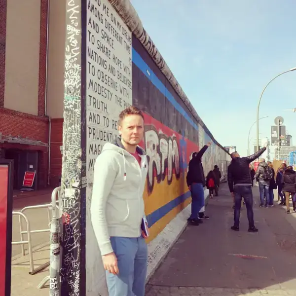Owain standing beside a painted section of the Berlin Wall