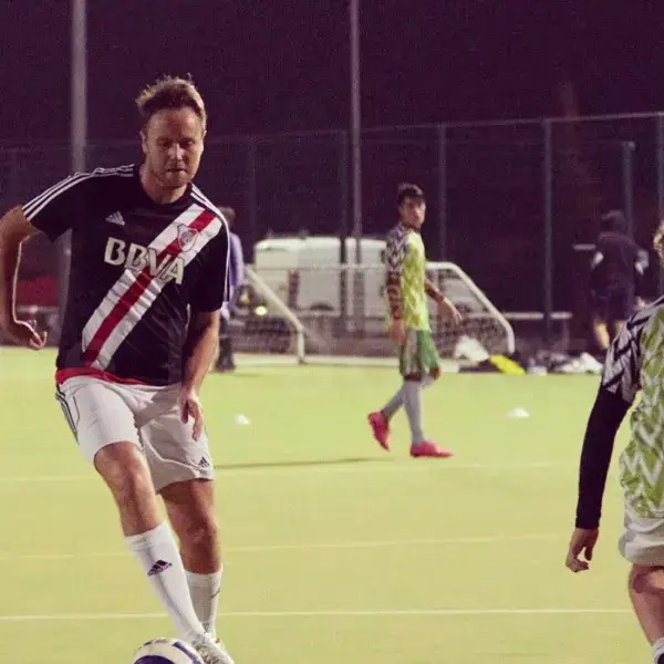Owain dribbling the ball in a River Plate style shirt under floodlights