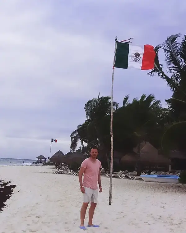 Owain on the beach beside a Mexican flag in Cancún