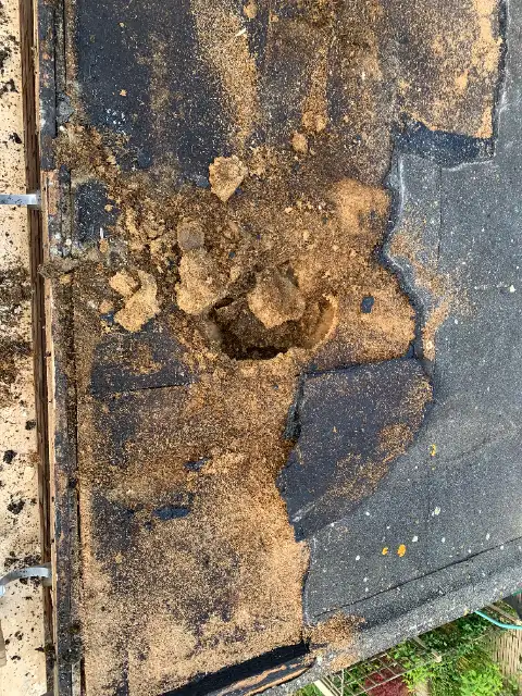 Eroded chipboard roof deck exposed under the felt