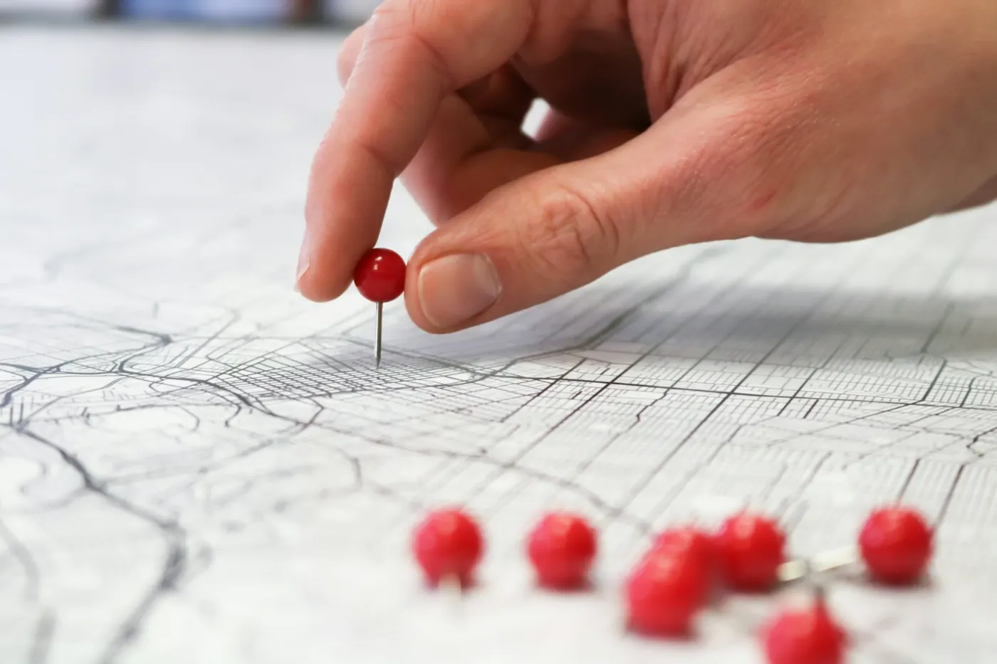 A hand placing a red pin on a street map