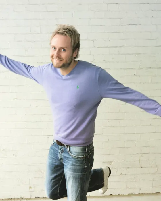 Owain with arms outstretched against a white brick wall in Shoreditch