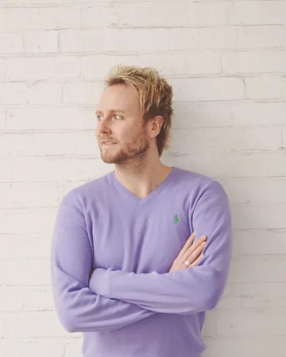 Owain with arms folded against a white brick wall in Shoreditch