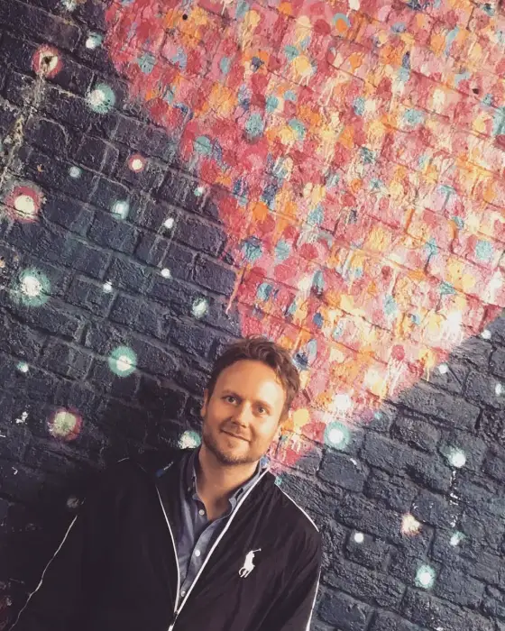 Owain in front of a painted brick mural in Shoreditch